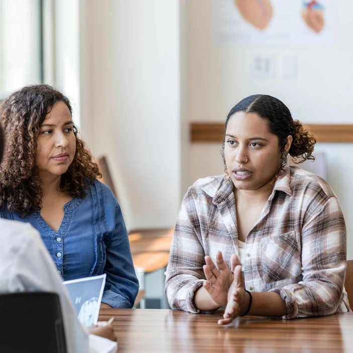 Deux femmes discutent avec une professionnelle dans un bureau lors d’une rencontre de type conseil d’école.